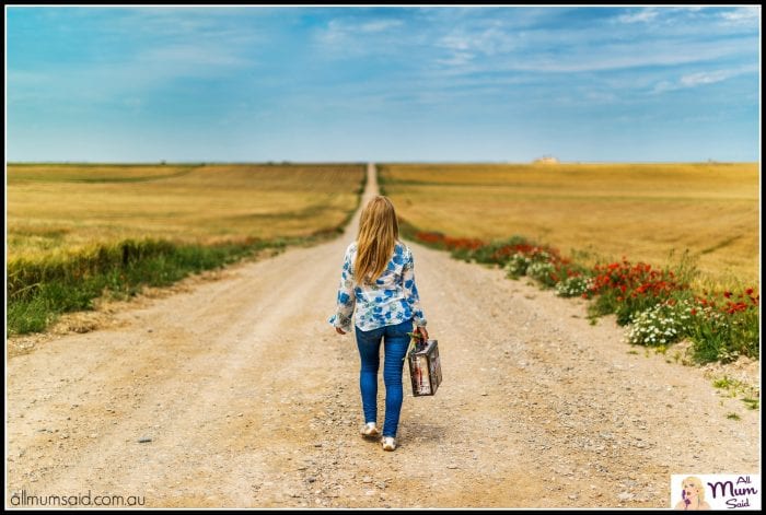 Packed suitcase woman walking down dirt road going on holidays