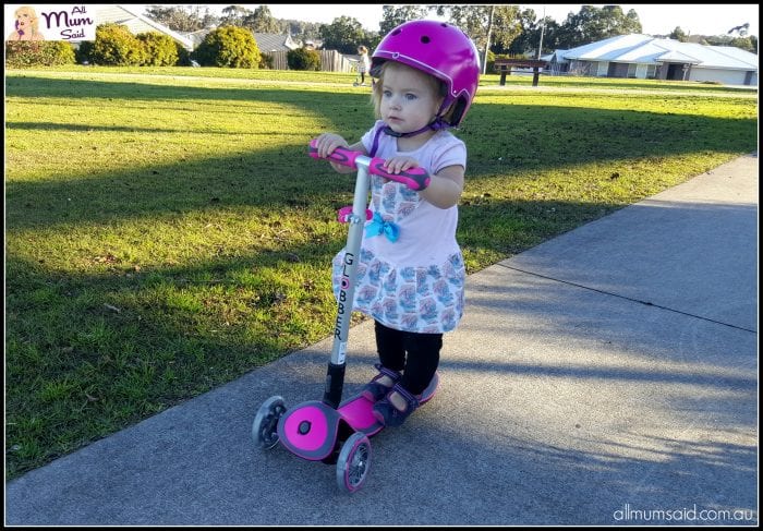 Toddler riding globber scooter and wearing globber helmet at park